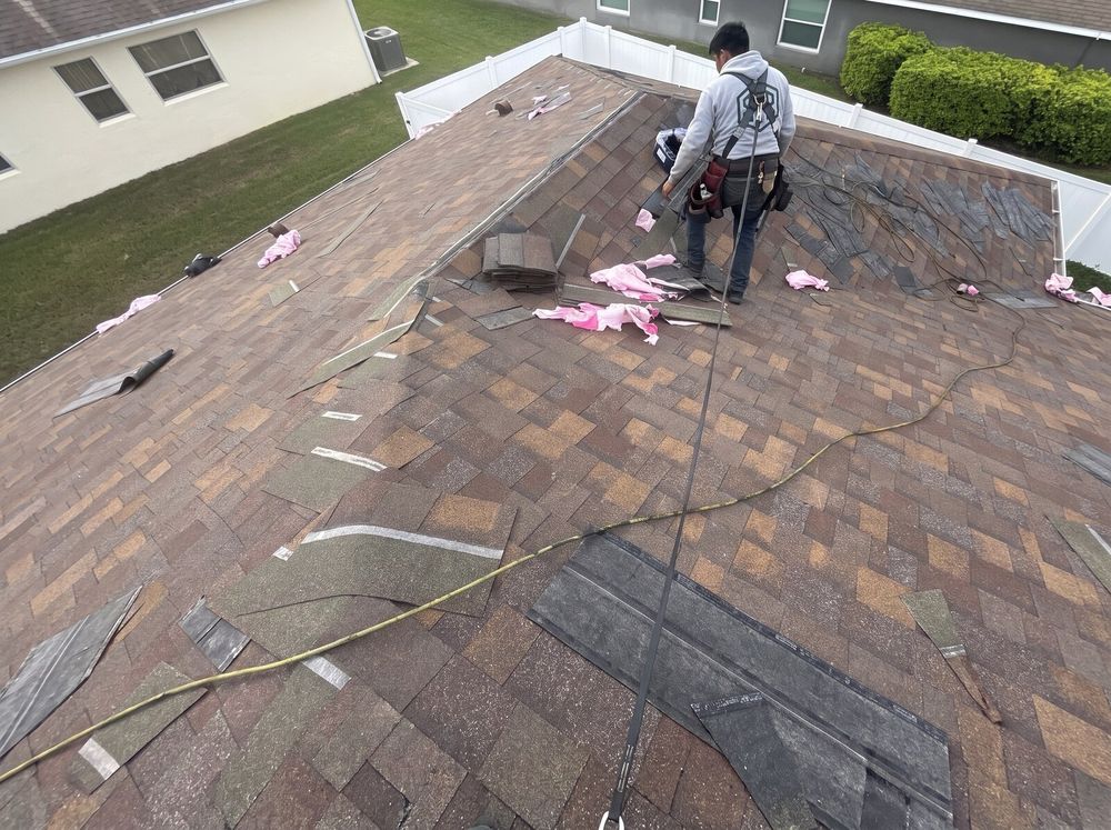 A roofer in an SFR hoodie and harness working at the hip during a shingle tear-off