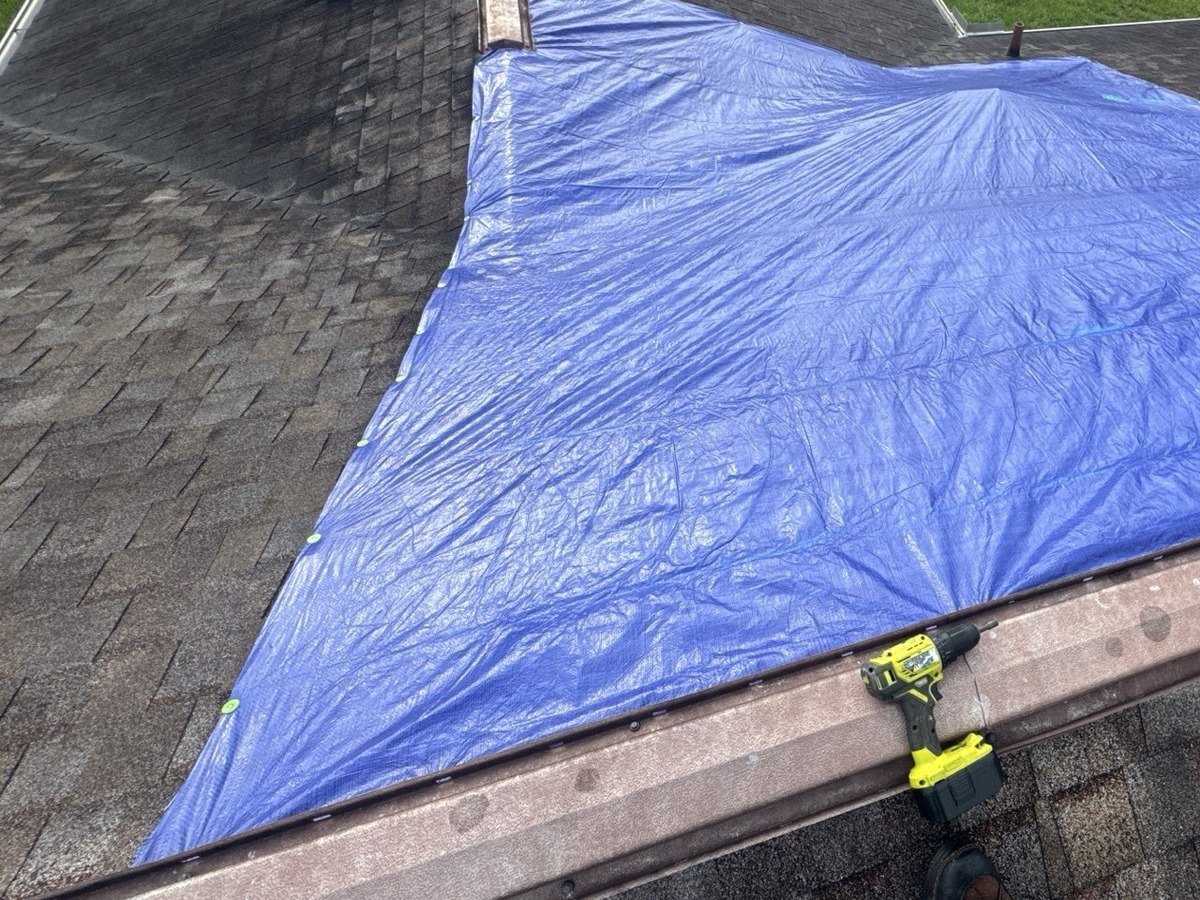 An emergency tarp fastened over a section of shingle roof to stop the water