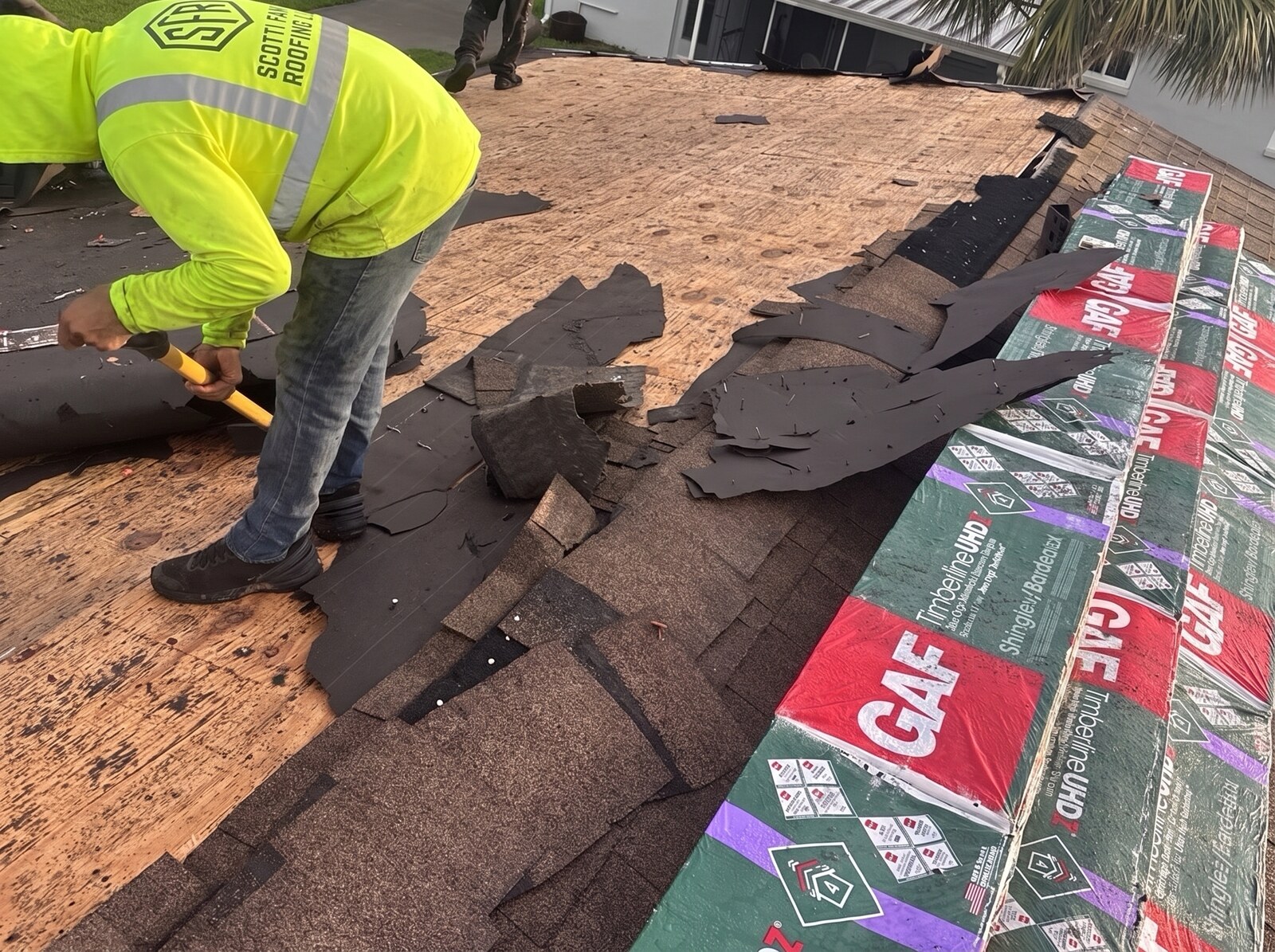 Scotti Family Roofing roofer clearing old shingles beside GAF Timberline bundles on a Beverly Hills FL roof