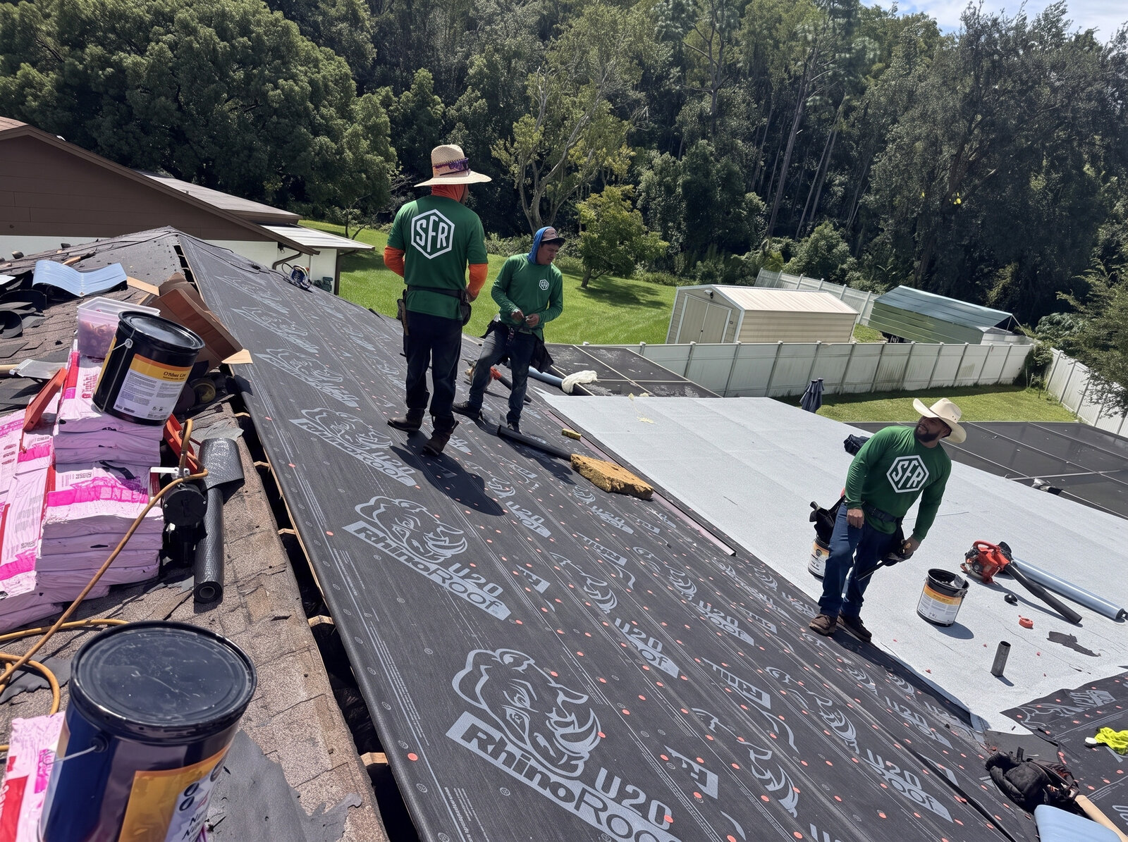 Three Scotti Family Roofing crew members rolling synthetic underlayment across a Tampa FL roof deck