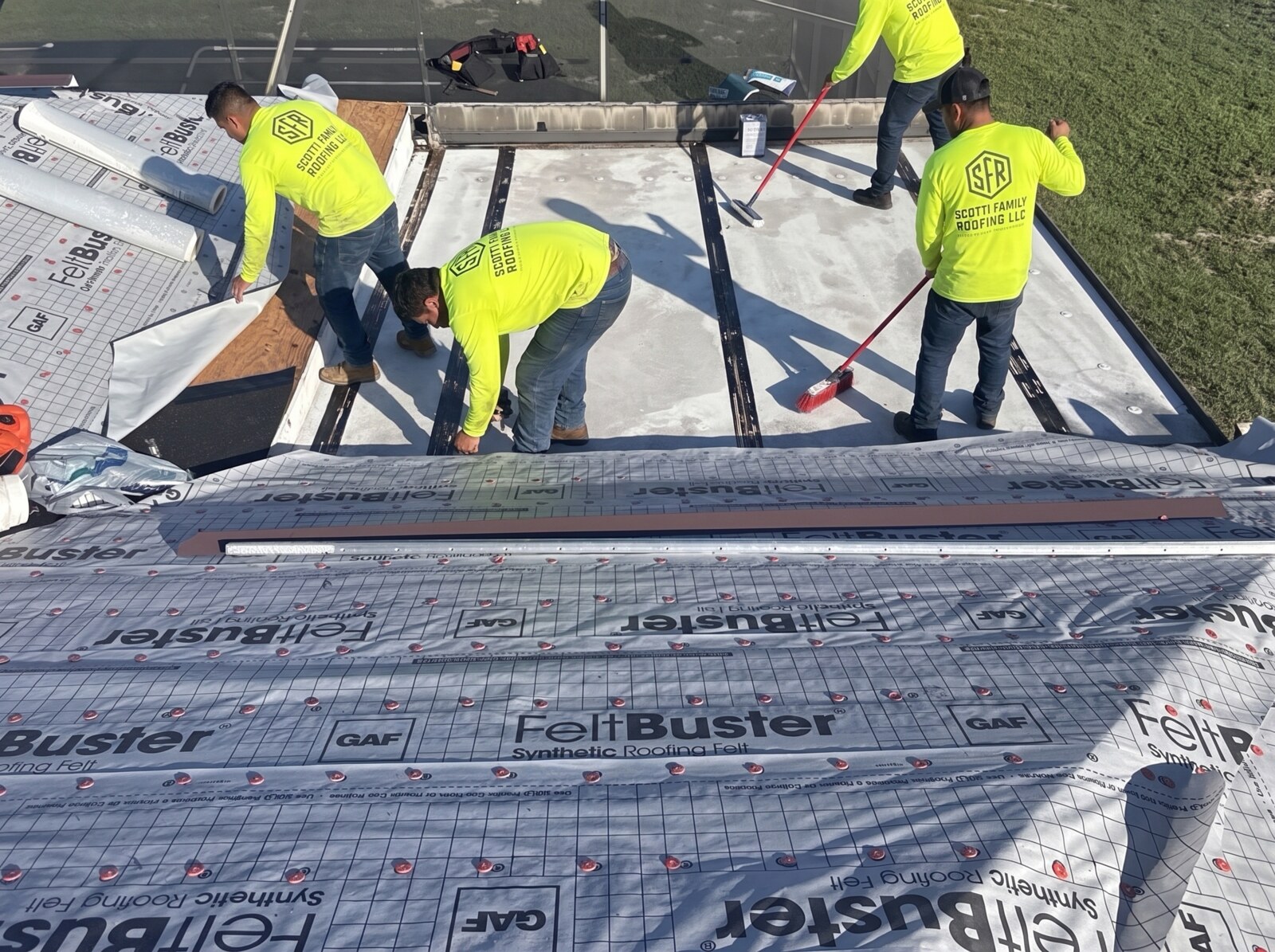 Three Scotti Family Roofing crew members installing GAF FeltBuster underlayment on a Spring Hill FL roof